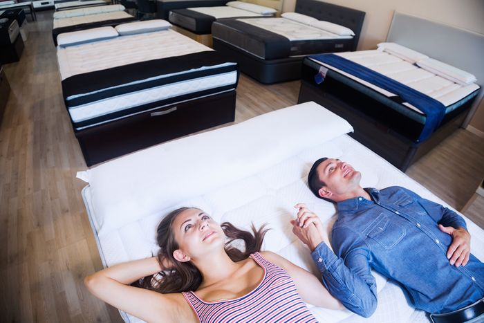 A young couple lie together on a test mattress in a mattress shop, holding hands.